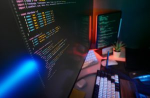 Ambiente real de desenvolvimento de software com computadores e telas de código, fotografia de Jakub Żerdzicki no Unsplash