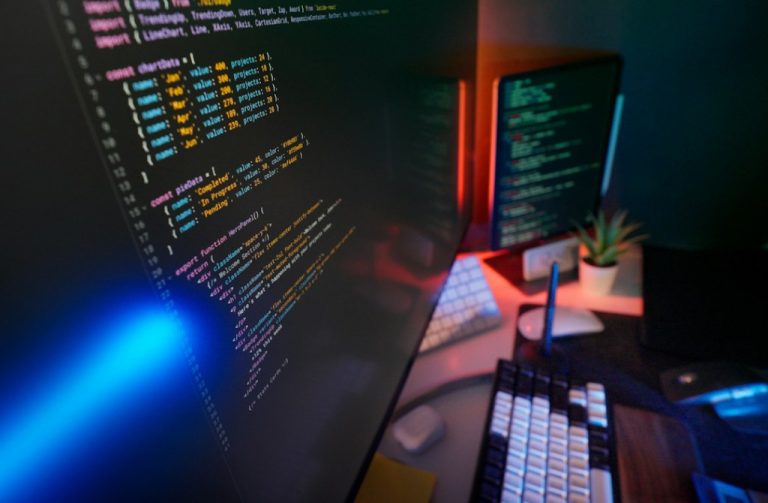 Ambiente real de desenvolvimento de software com computadores e telas de código, fotografia de Jakub Żerdzicki no Unsplash